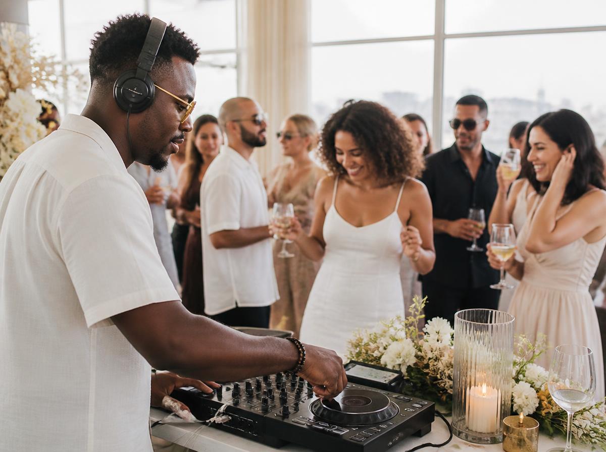 A Black DJ performing mid-set in bright daylight as a diverse crowd of guests dances and celebrates